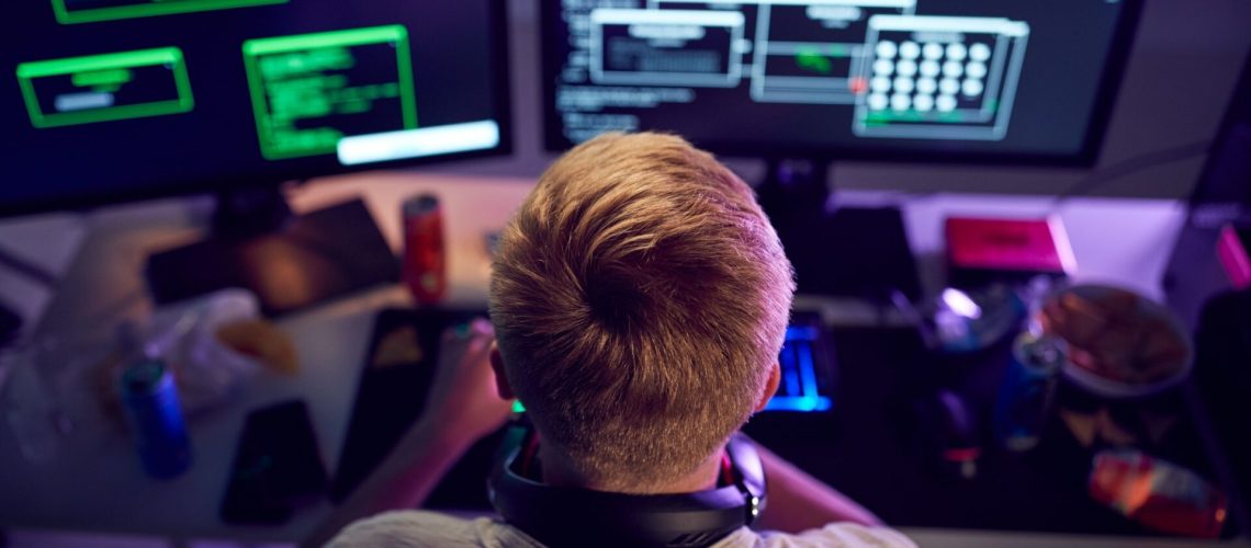 Male Teenage Hacker Sitting In Front Of Computer Screens Bypassing Cyber Security